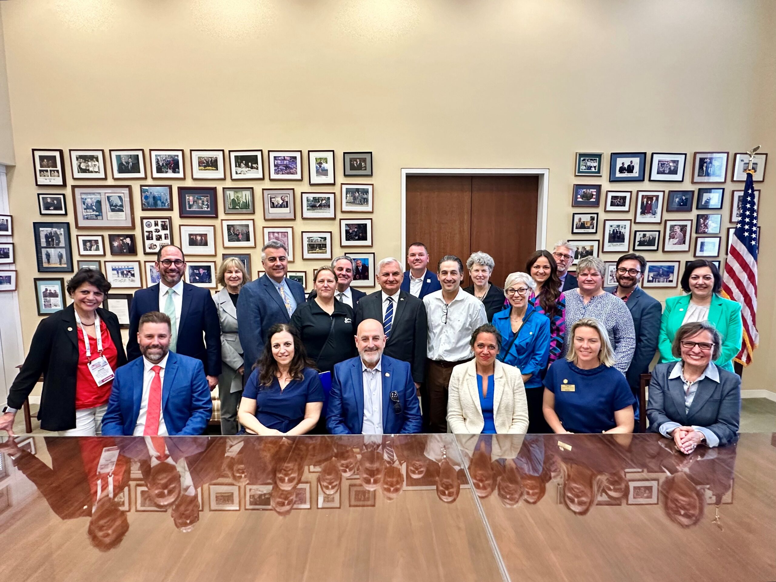 Photo of large group with pictures on the wall behind them at conference table